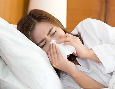 Woman sneezing in tissue on a bed and having difficulty sleeping because of a stuffy nose