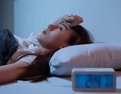 A woman lying unable to sleep with a clock on her bedside, emphasizing the late hours