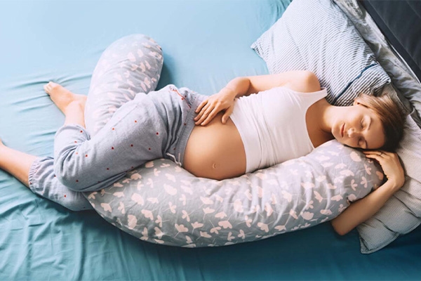 A pregnant woman sleeping on her side wrapped around a full-body pregnancy pillow