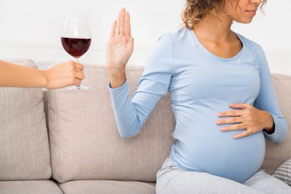 A pregnant gesturing her hand to refuse wine consumption during pregnancy.