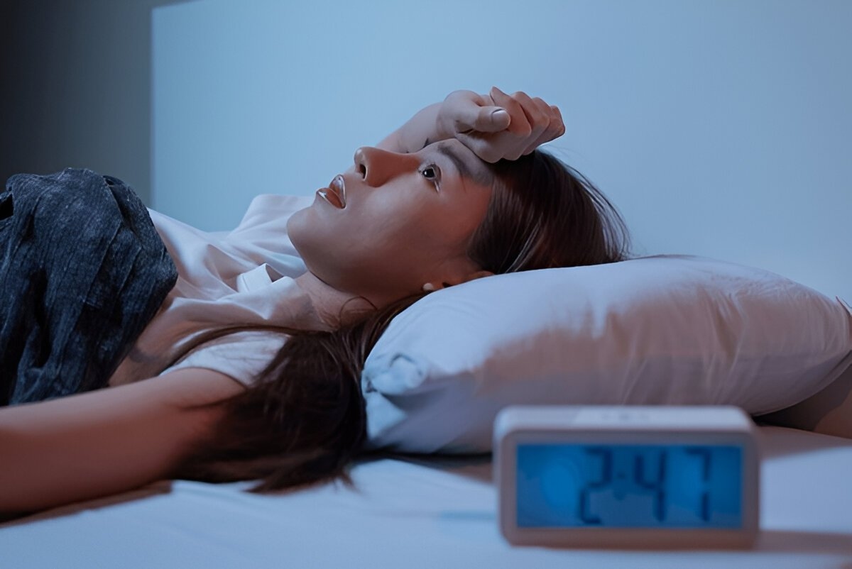 A woman lying unable to sleep with a clock on her bedside, emphasizing the late hours