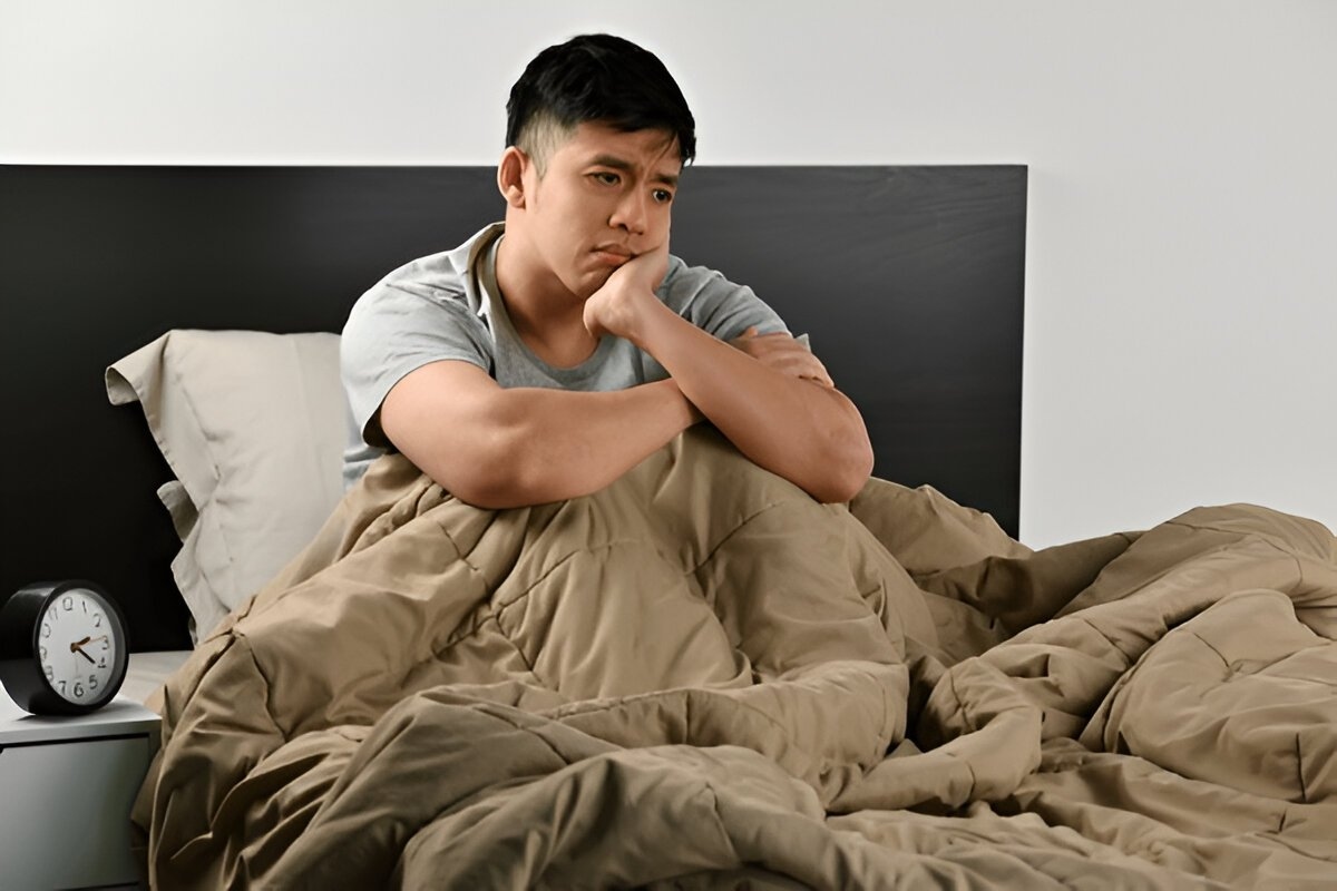 A man sitting on his bed restless, unable to fall asleep once awake