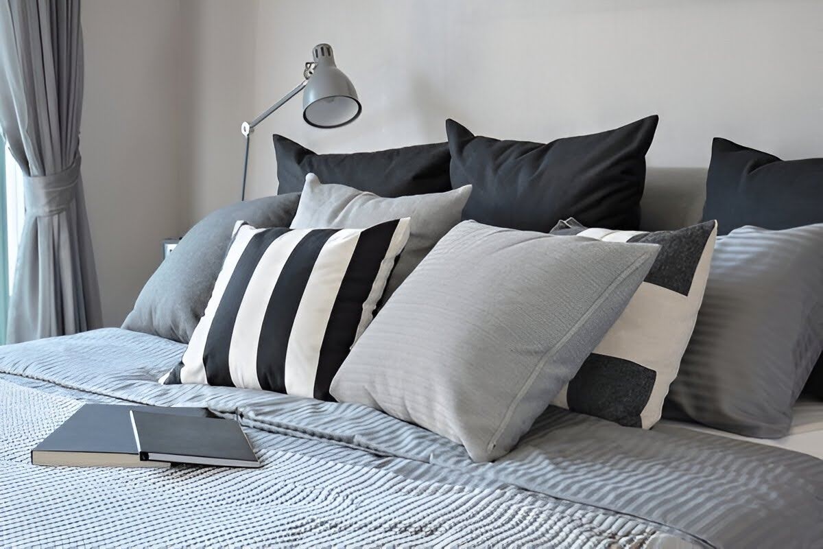 A couple of pillows neatly placed on a bed, with a lamp and notebooks kept on the side