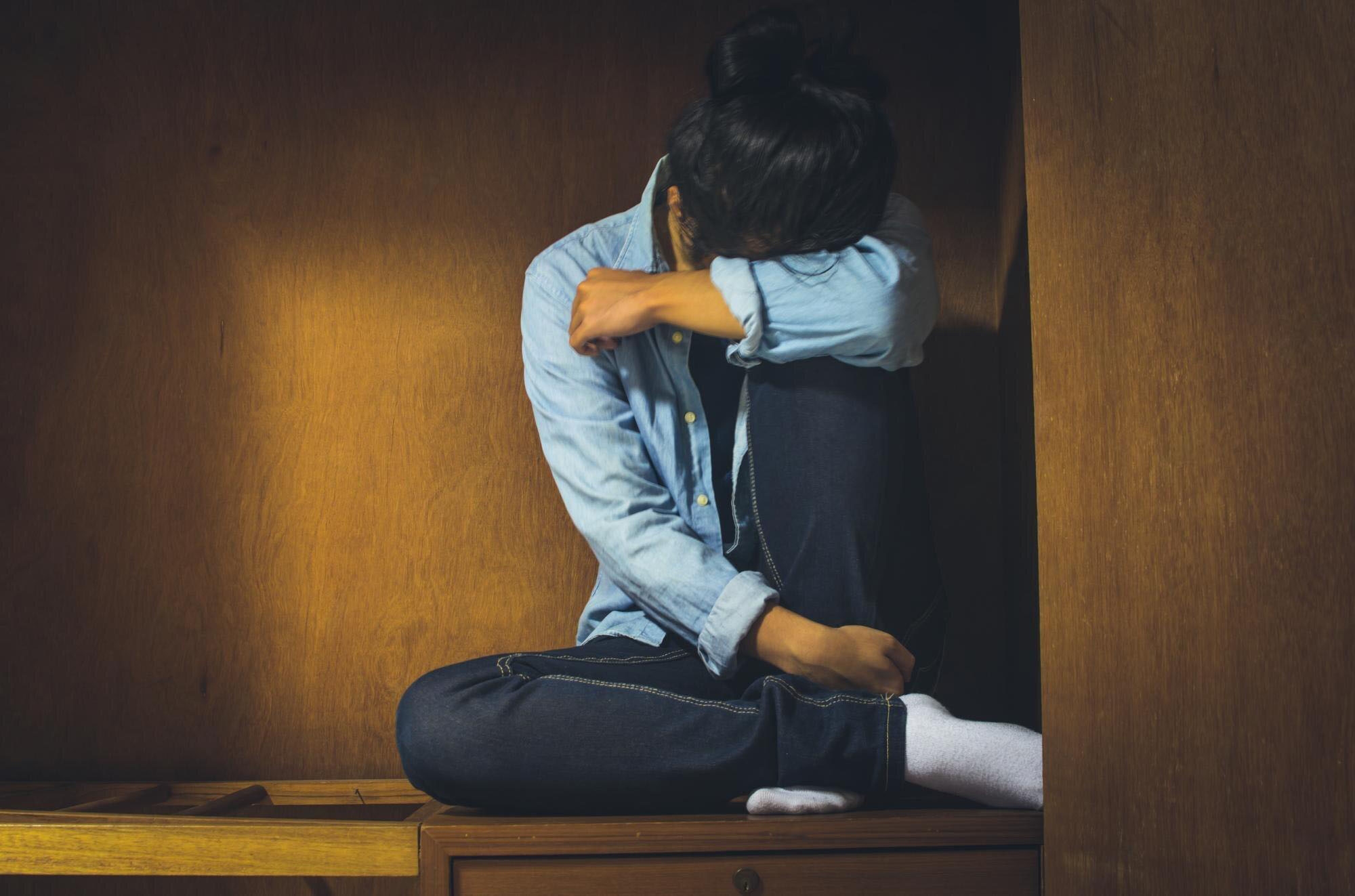 A young woman seated on a wooden bench in a room, symbolizing the struggles of women with post-traumatic stress disorder