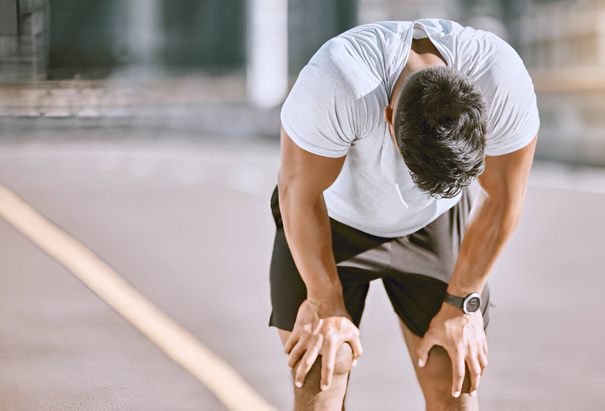 A man with a knee injury rests on the roadside, appearing uncomfortable and in need of medical attention